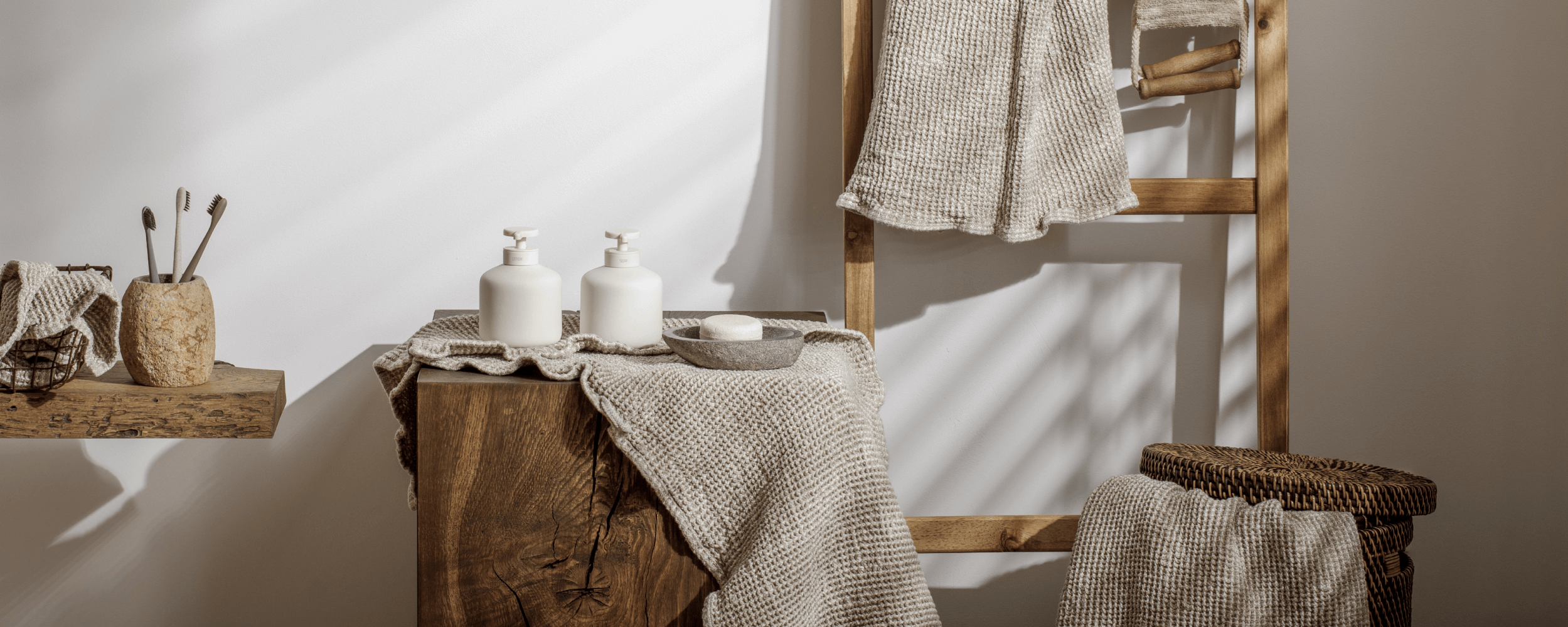 Bathroom setting with wooden stool, towels, and toiletries against a neutral wall.