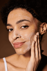 Woman applying a skincare product to her face with a neutral background